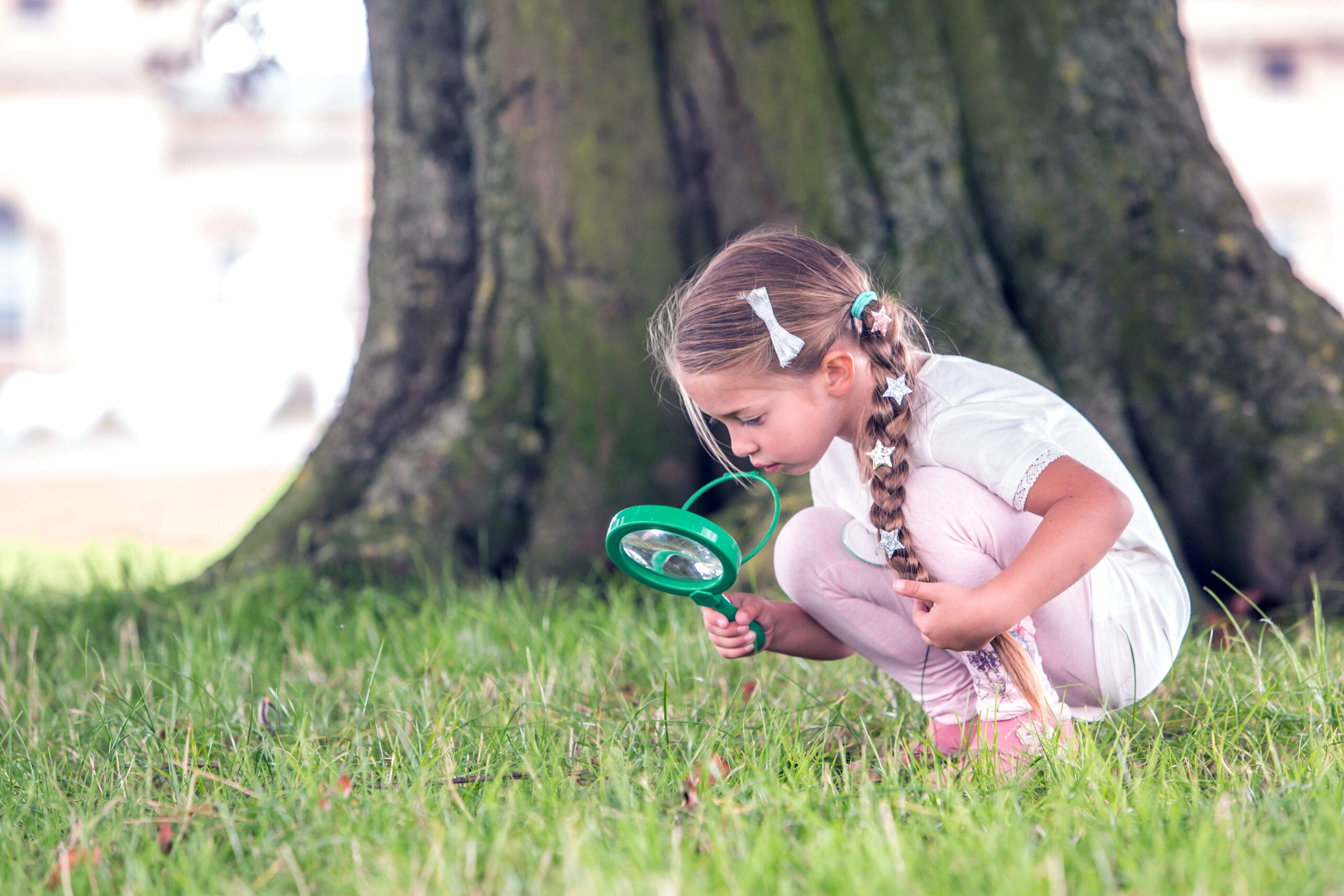 Girl outdoors looking at grass with magnifying glass