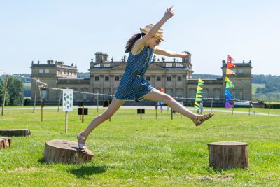 Girl jumping across logs in front of Harewood House