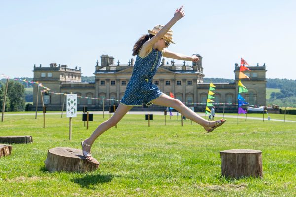 Girl jumping across logs in front of Harewood House