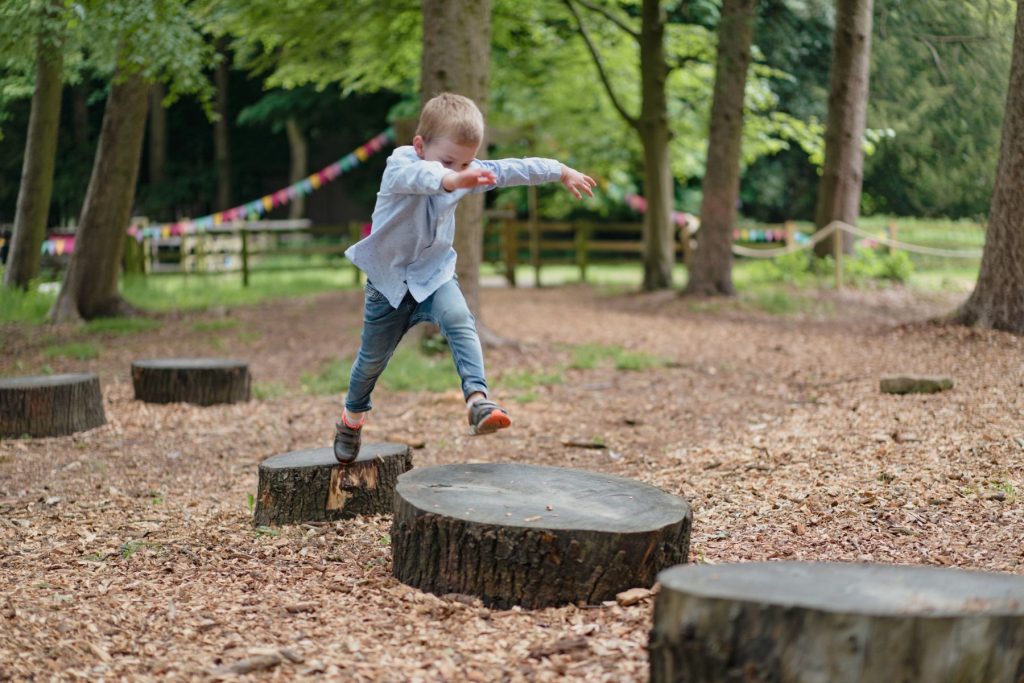 small child jumping across tree trunk stepping stones