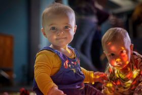 two young babies look directly at camera illuminated by various neon lights