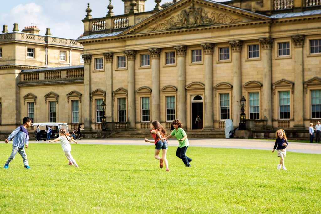 Children run and play on the lawn in front of Harewood House