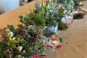 a series of plant pots laid across a table with different types of holly, spruce and tealights