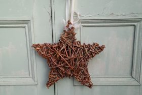 A chunky star made of willow, hanging on a white door by a white ribbon.