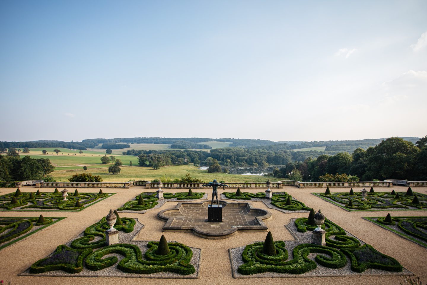 Clear blue skies sit above the rolling Capability Brown landscape with trees dotted across the horizon. Orpheus stands proudly in the middle of an ornate pool of water on the Victorian Terrace.