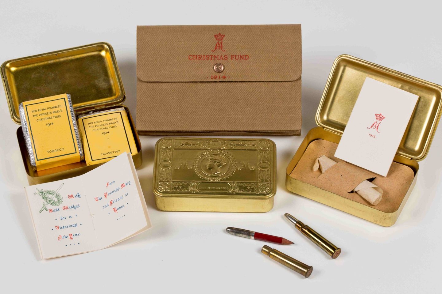 A selection of embossed brass Christmas gift boxes showing their contents, including tobacco packets, bullet case pencils and christmas cards from Princess Mary.